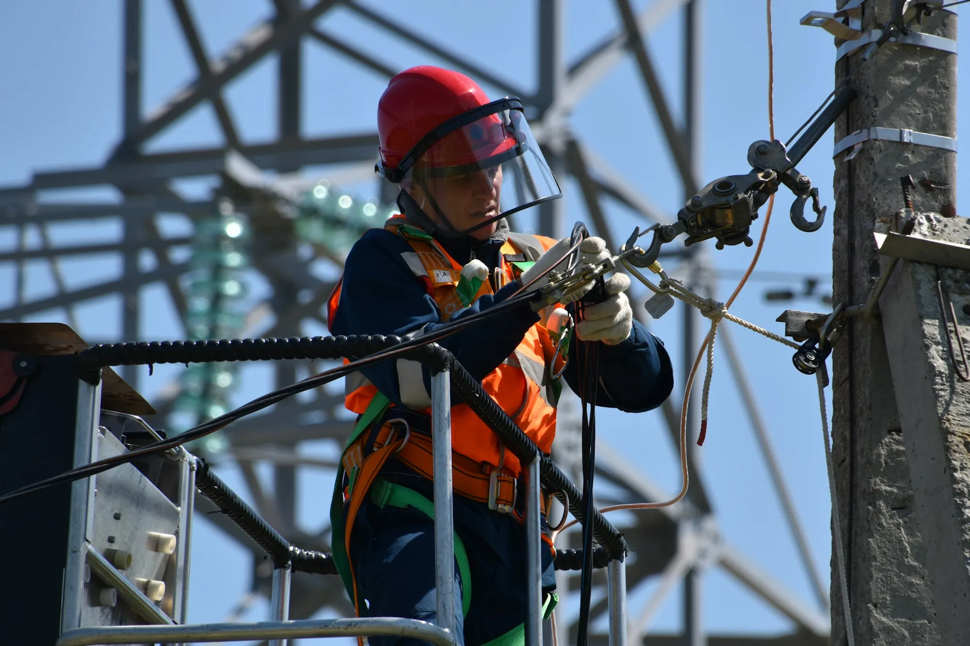 Line worker in a red hard hat and face shield working on overhead power equipment